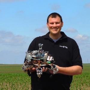 David Dorhout holds a robot while standing in a field
