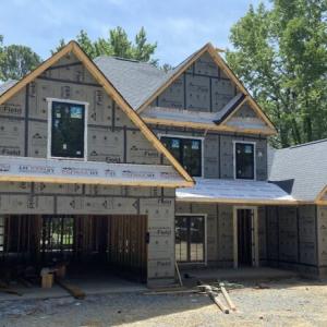 A two-story home being built. Dense trees behind it.