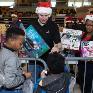 Volunteers in santa hats handing out toys to kids in a large auditorium.