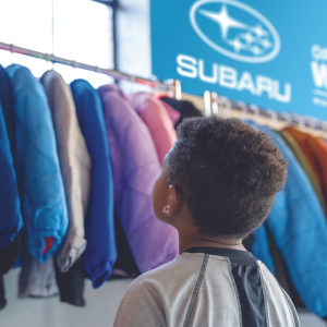child looks up at hanging coats