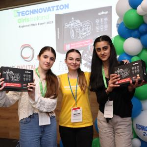 Three people standing together next to balloons, holding up boxes