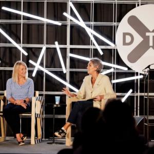 Two people seated on a stage. DTS logo displayed behind them.