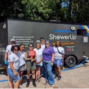 A small group of people posed together outside a ShowerUp mobile laundry unit