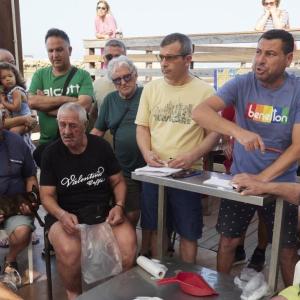 A group of people in a small auction, two speakers at the front.