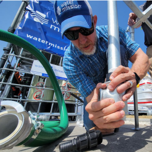 A person kneeling and connecting pipes outside.