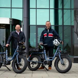 Pete Bowker and Daniel Usher posed by e-bikes outside a Northern Trust building.