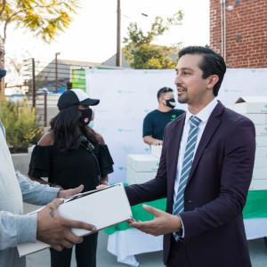 A man in a suit hands a Human-I-T box to a man in a mask