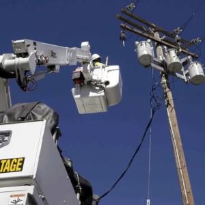 SCE troubleman Paul Chhay is lifted by a bucket truck to complete a repair job.