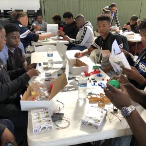 Students sit at a table assembling pieces of electronic equipment