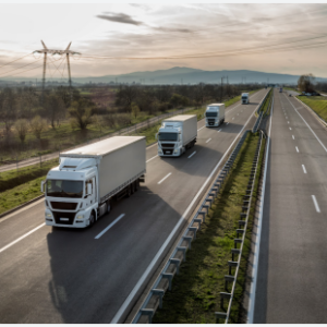 A line of semi trucks going down a road, wind turbines in the background.