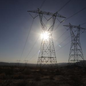 Tall power lines lined up with the sun over a large flat open landscape