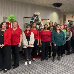 A group of volunteers posed in front of a chistmas tree. One dressed as the grinch behind them.