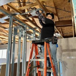 Maria on a ladder doing electrical work.