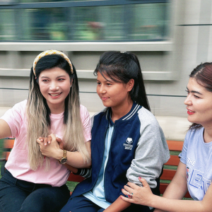 Three students sitting on a bench together and smiling