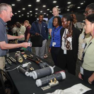 A person standing at a booth showing others parts.