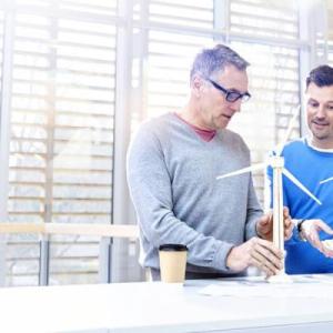 Two people holding small models of wind turbines in an open space.