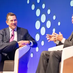 Two people seated, talking on a stage.