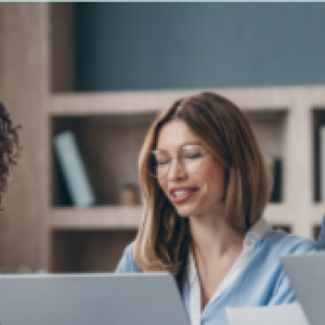 Four people posed in an office setting, some with open laptops.