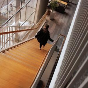 A person walking down a long, wooden, staircase.