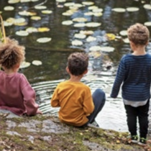 Three children playing on the bank of a waterway.