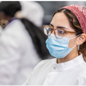 A person in ppe looking at a screen, others to their right doing the same