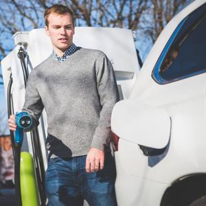 A person with a plug in one hand next to an open cover on an electric vehicle.