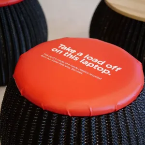 A black stool with Orange cushion "Take a load off on this laptop." printed on top.