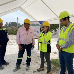 Four people in high-vis vests and hard hats talking under a canopy