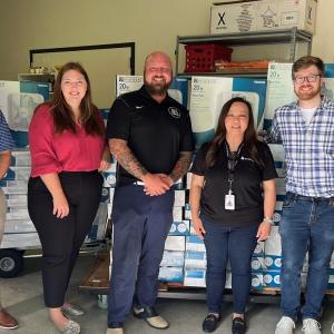 A group of five posed in front of stacks of boxed fans.