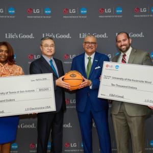 Four people posing with two oversized checks and a basketball
