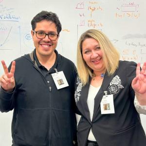 Two people standing together, making peace sign gestures