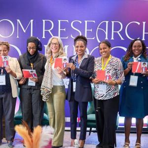 Eight people on a stage, each holding up the same photo