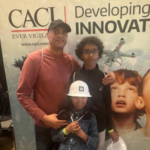 A group of three posed in front of a CACI banner