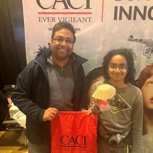 Two people in front of a CACI banner, holding up a CACI bag.