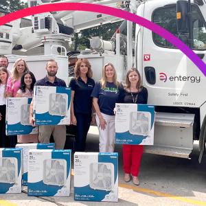 People posed outside with boxed fans in front of an Entergy bucket Truck.