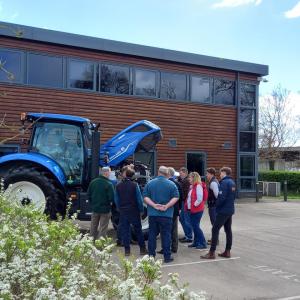 A small group of people gathered around a New Holland tractor in a parking lot.