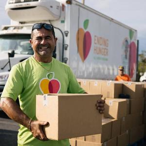 A person holding a box, a stack of boxes and truck behind them