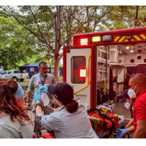 People helping lift a stretcher behind an ambulance.