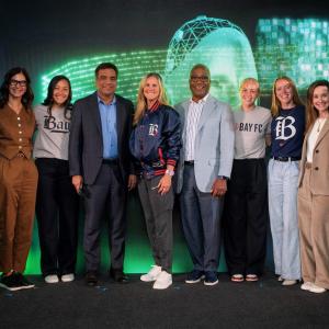 A standing group of people posed together in front of a dark screen with bright green digital symbols.