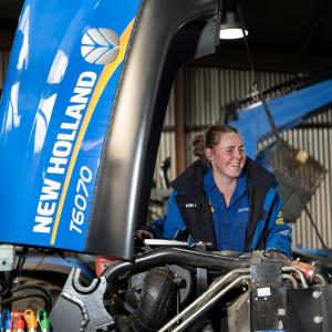 A smiling person looking under the hood of a farming tractor.