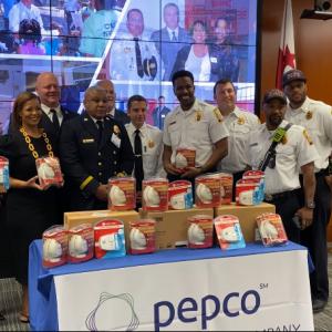A group of people, some in fire/EMS uniform, behind a table of smoke detectors and a pepco banner.