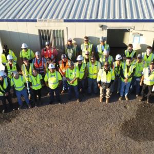 a large team of people, all wearing safety gear, outside a mobile trailer.