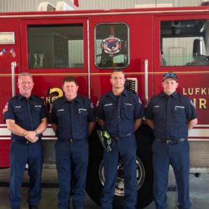 A row of people, some in uniform, in front of a fire truck.