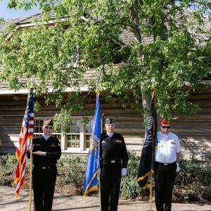 Three people in uniform holding flags to their side.
