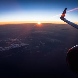 passenger view of the wing of a plane, the sun setting in the horizon