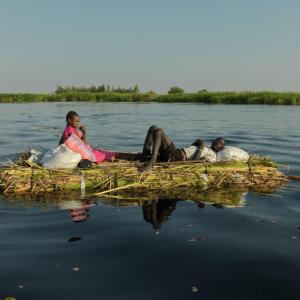 A man and wife float down the White Nile on a grass mound. They hope to reach New Fangak with the current of the river.