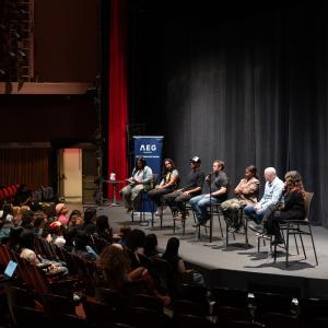 Panelists seated onstage speaking to an audience in a theater, with AEG Presents College Connection Program signage beside the stage.