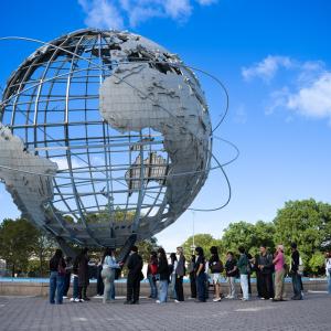 Group gathers outdoors beneath the Unisphere at Flushing Meadows Corona Park under a bright blue sky.