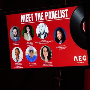 Large screen displays an AEG Presents “Meet the Panelist” graphic featuring photos, names and titles of seven panel participants.