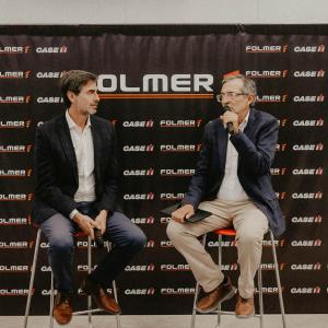 Two people in chairs, one talking into a microphone